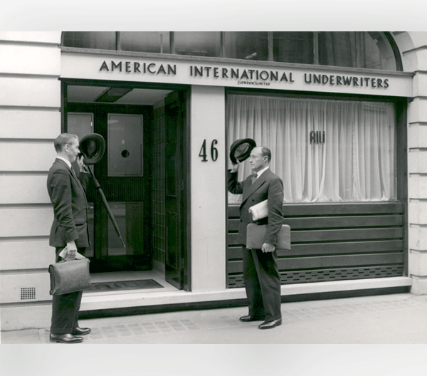 Two men greeting each other in front of an American International Underwriters office in the United Kingdom