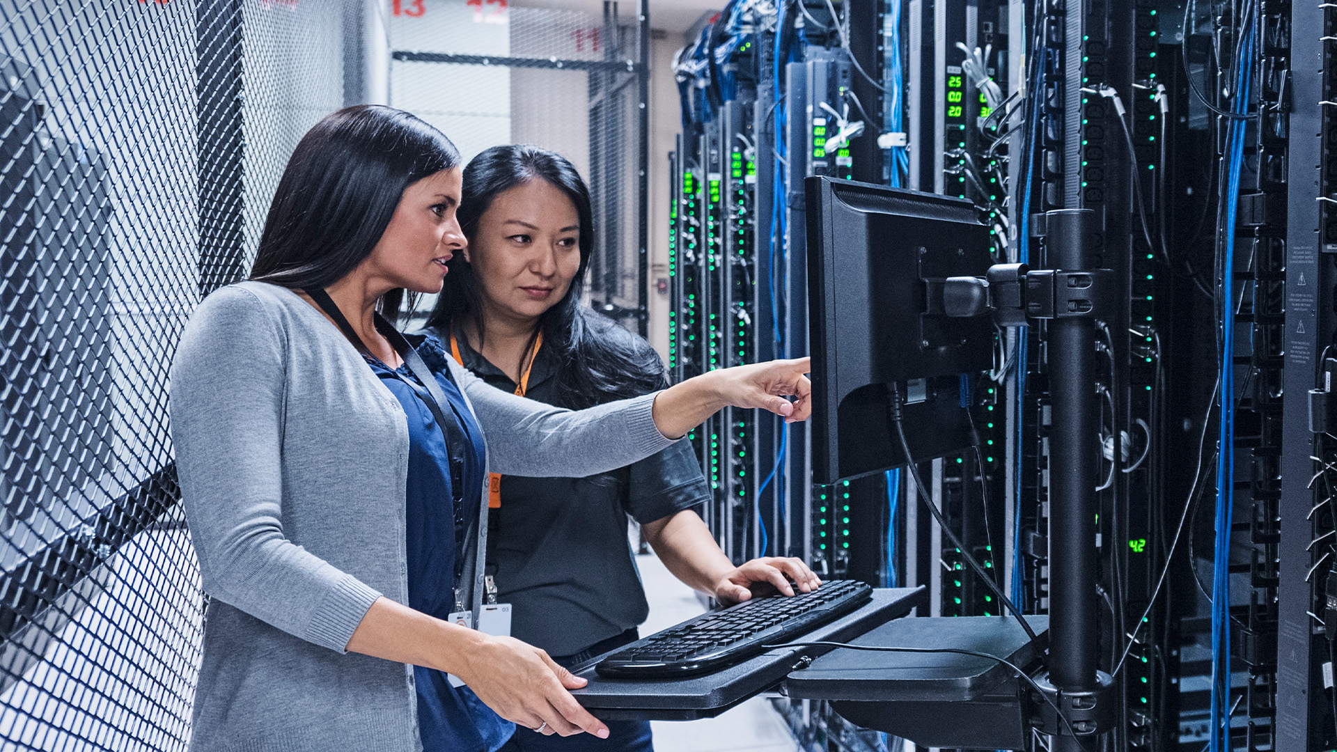 Two women in a server room, viewing a monitor screen